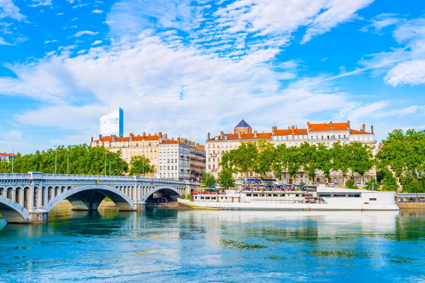 Vue panoramique du pont de Lyon sur le Rhône avec immeubles haussmanniens et bateau amarré sous un ciel bleu.
