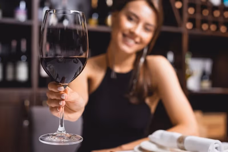 Femme souriante tenant un verre de vin rouge dans un bar à vin à Split, Croatie