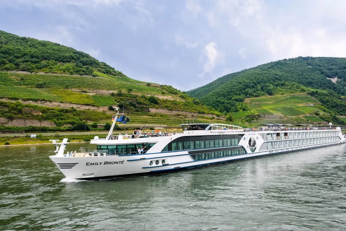 Bateau de croisière naviguant sur le Rhin, entouré de collines verdoyantes et de vignobles en terrasses dans la vallée du Rhin romantique.
