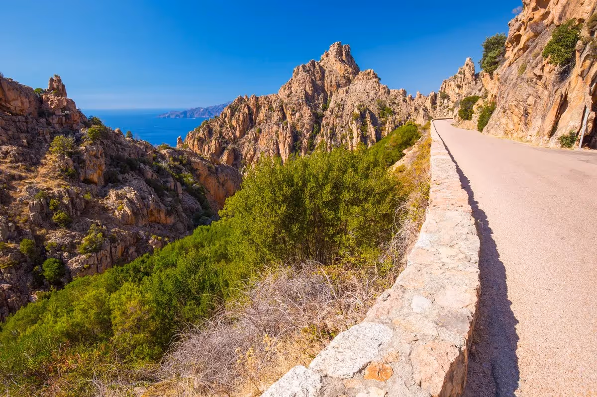 Route sinueuse dans les calanques de Piana, en Corse, surplombant la mer Méditerranée et les falaises rocheuses typiques de l’île de Beauté.
