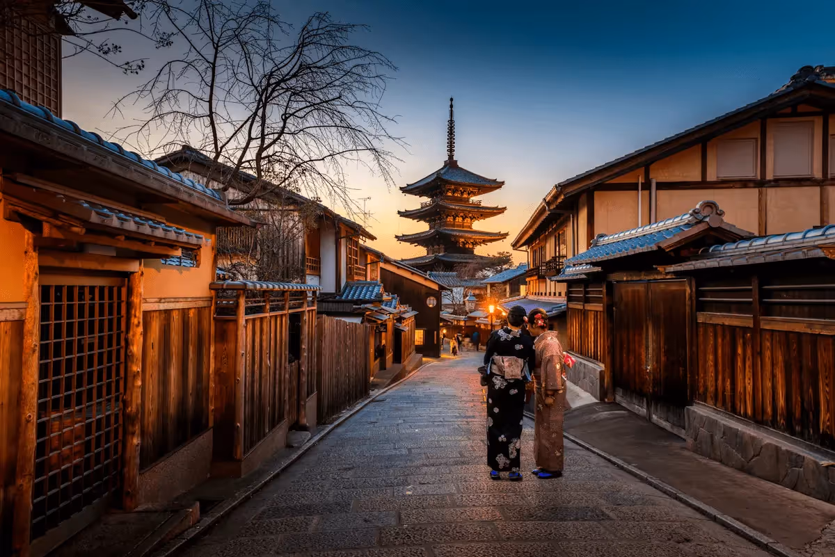 Rue traditionnelle de Kyoto au coucher du soleil avec deux femmes en kimono et une pagode en arrière-plan.