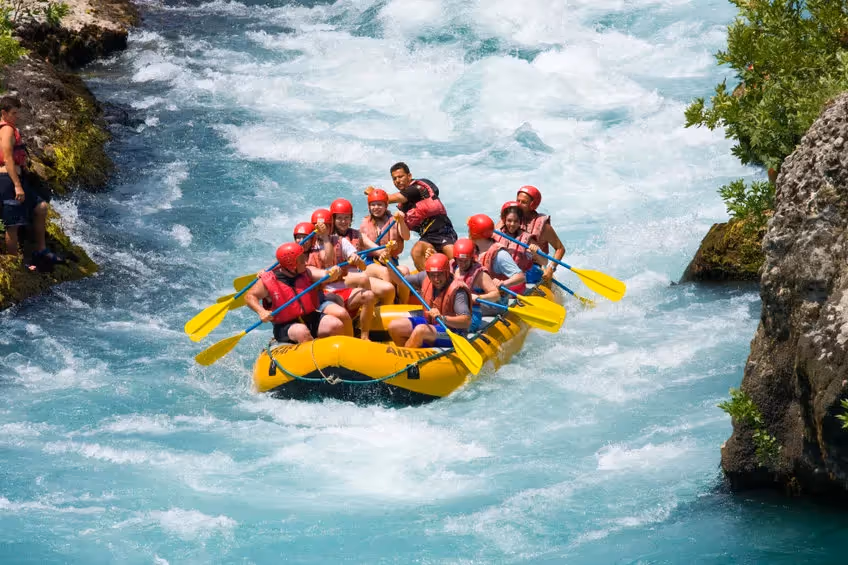 Équipe en rafting sur une eau turquoise agitée, portant casques rouges et gilets de sauvetage, dans un canot gonflable jaune encadré de rochers.