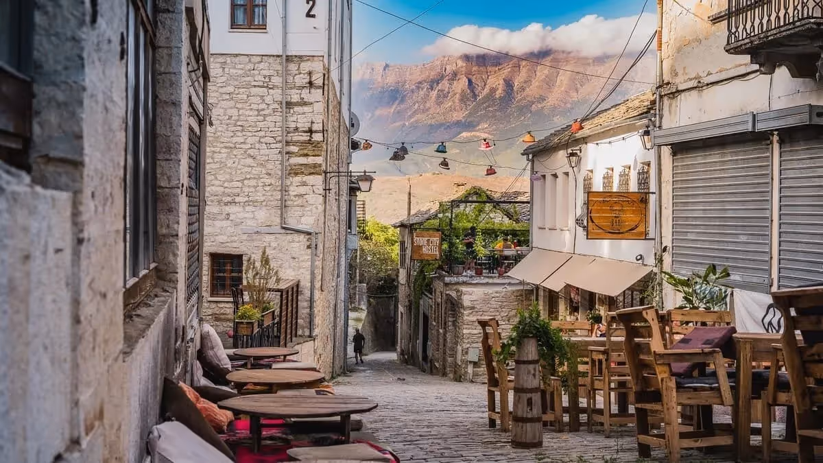 Ruelle pavée de Gjirokastër bordée de maisons traditionnelles et de terrasses, avec vue sur les montagnes albanaises