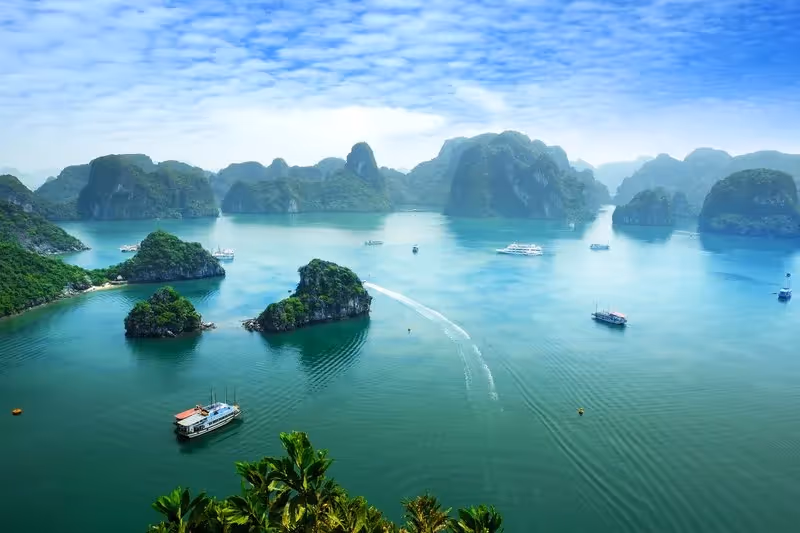 Vue panoramique sur la baie d’Halong avec ses formations karstiques spectaculaires et des bateaux de croisière naviguant dans une mer turquoise.