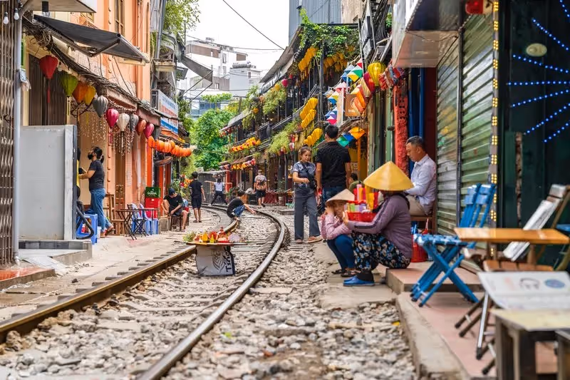 Rue emblématique de Hanoï traversée par une voie ferrée, bordée de cafés et lanternes colorées, avec des habitants et touristes en activité.
