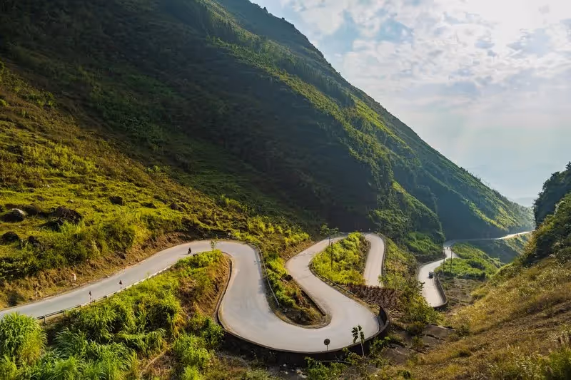 Route sinueuse traversant les montagnes verdoyantes de Hà Giang au Vietnam, baignée par la lumière matinale.