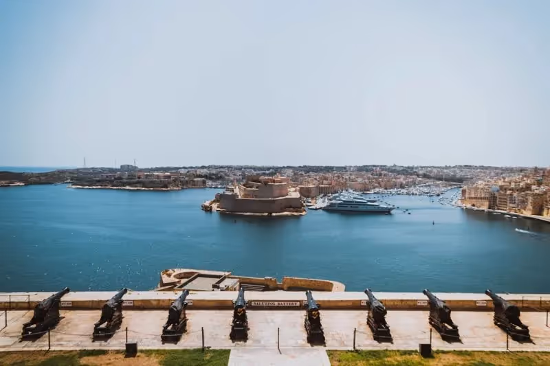 Vue depuis la Saluting Battery à La Valette, Malte, avec des canons alignés surplombant le Grand Harbour et une ancienne forteresse en contrebas.