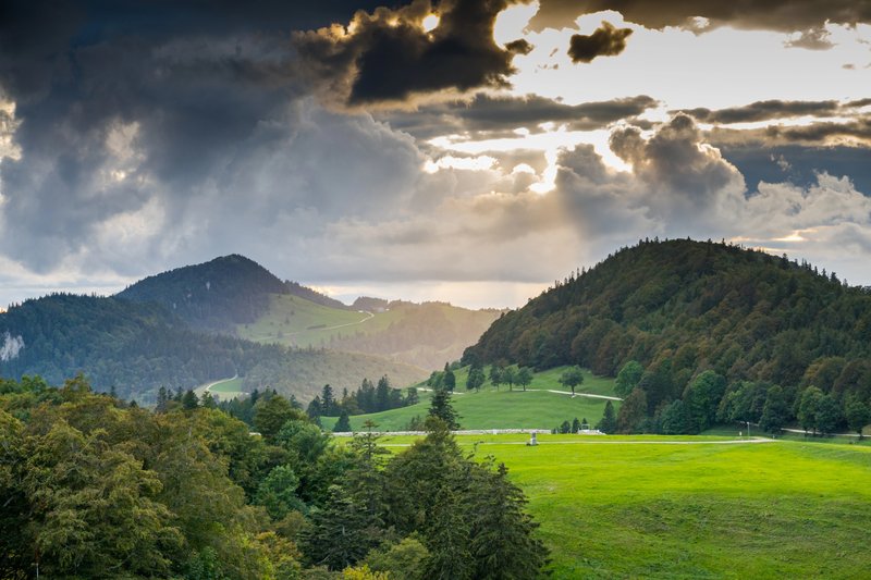 Paysage vallonné du Jura français avec collines boisées et lumière perçante à travers les nuages, parfait pour une micro-aventure nature.