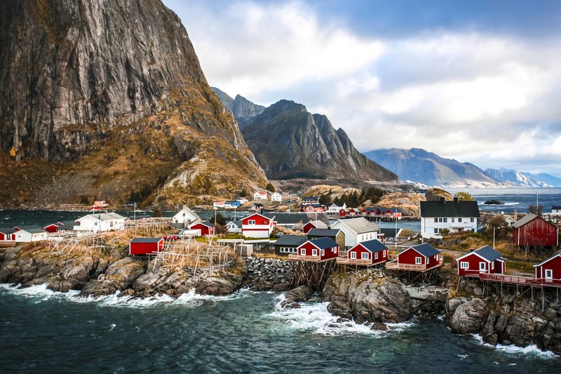 Cabanes rouges de pêcheurs à Hamnøy, dans les îles Lofoten en Norvège, au pied d’une falaise spectaculaire face à la mer.