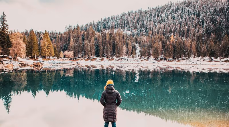 Personne contemplant un lac de montagne en hiver, entouré de forêts enneigées, illustrant la quiétude du slow travel en nature.