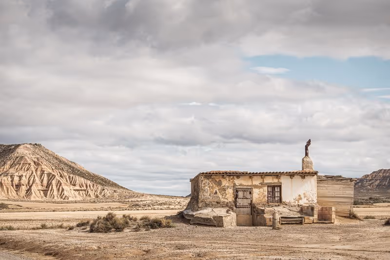 Vieille cabane en pierre dans le désert des Bardenas Reales, avec collines arides en arrière-plan et ciel nuageux.