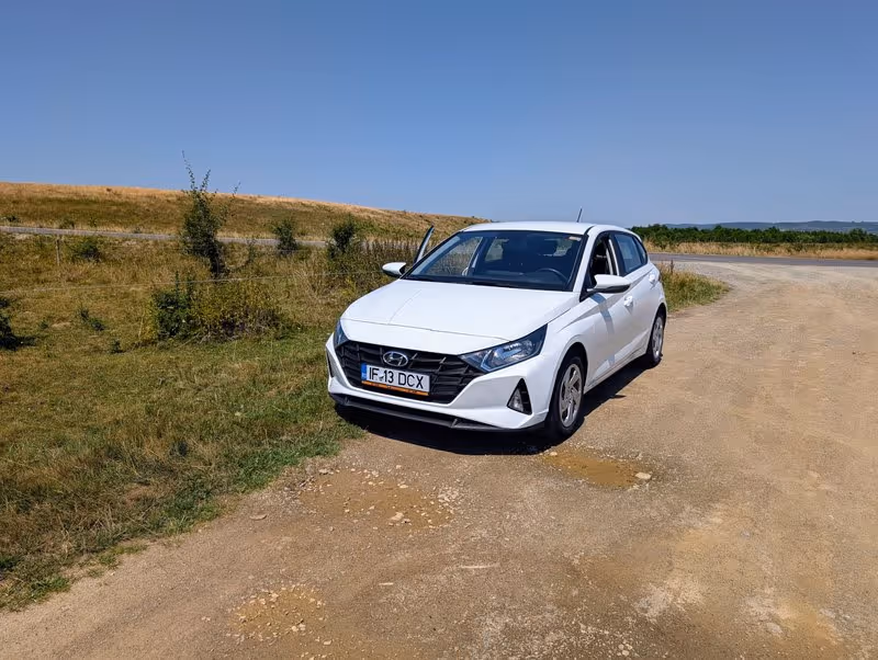 Voiture de location blanche garée sur un chemin de terre en pleine campagne roumaine, sous un ciel dégagé.