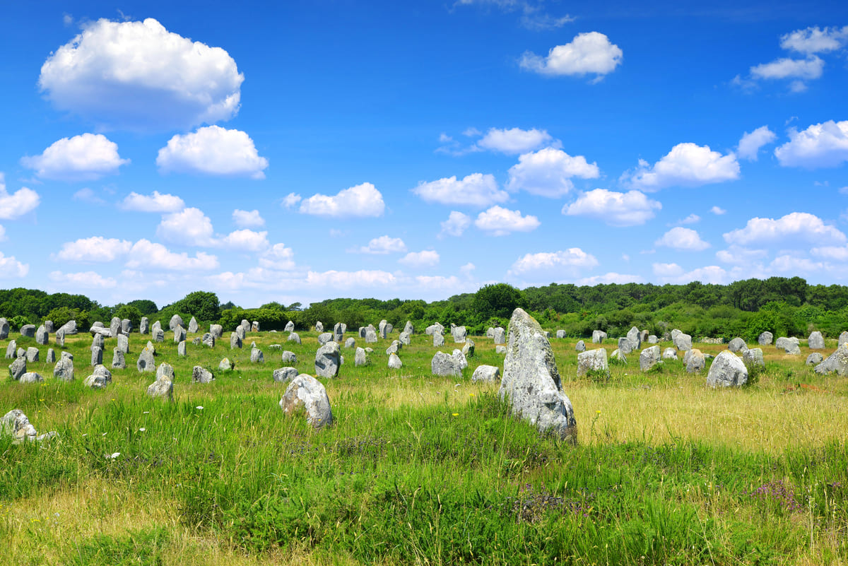 Vue panoramique des alignements de menhirs à Carnac, en Bretagne, sous un ciel bleu parsemé de nuages.