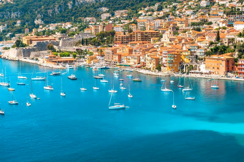 Vue panoramique de Nice avec ses maisons colorées et ses voiliers sur la Méditerranée.