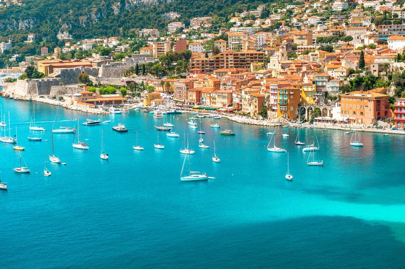 Vue panoramique de Nice avec ses maisons colorées et ses voiliers sur la Méditerranée.