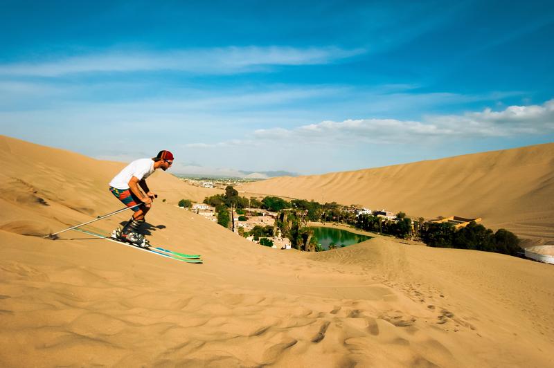 Voyageur pratiquant le sandboard sur les dunes de Huacachina avec vue sur l’oasis.