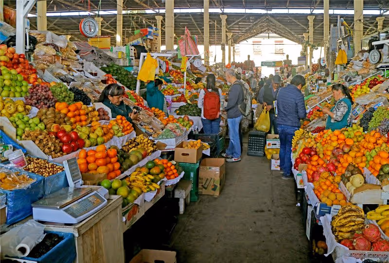 Étals de fruits colorés au marché San Pedro de Cusco, avec habitants et visiteurs faisant leurs courses