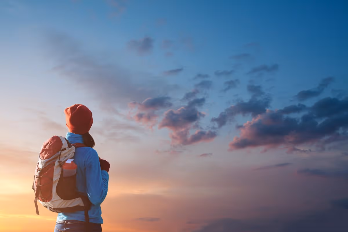 Personne portant un sac à dos regardant un ciel coloré au coucher du soleil.