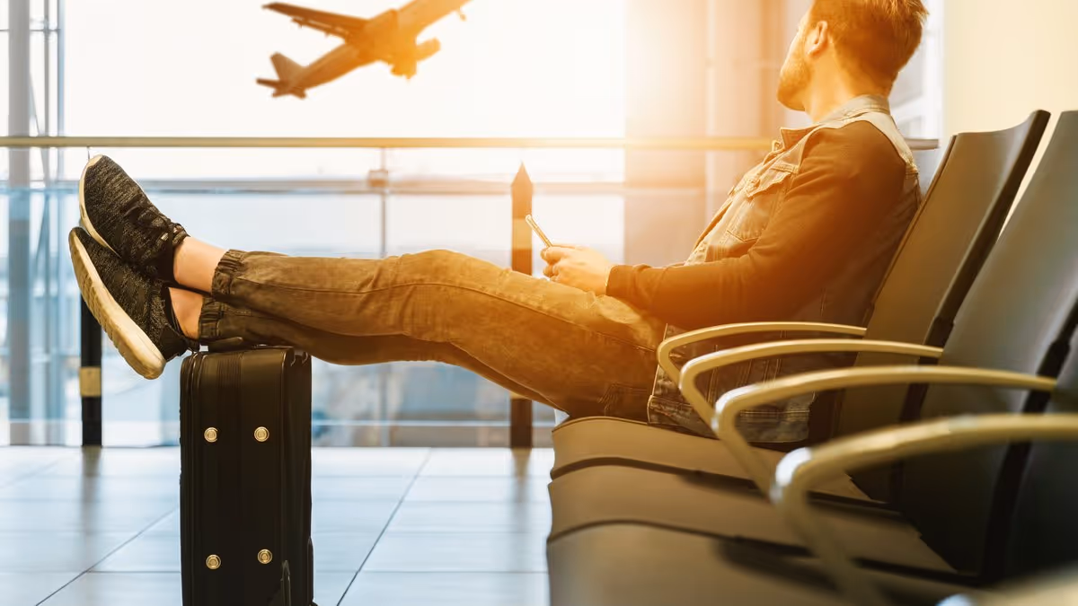 Voyageur assis dans un aéroport, regardant un avion décoller avec ses jambes posées sur une valise