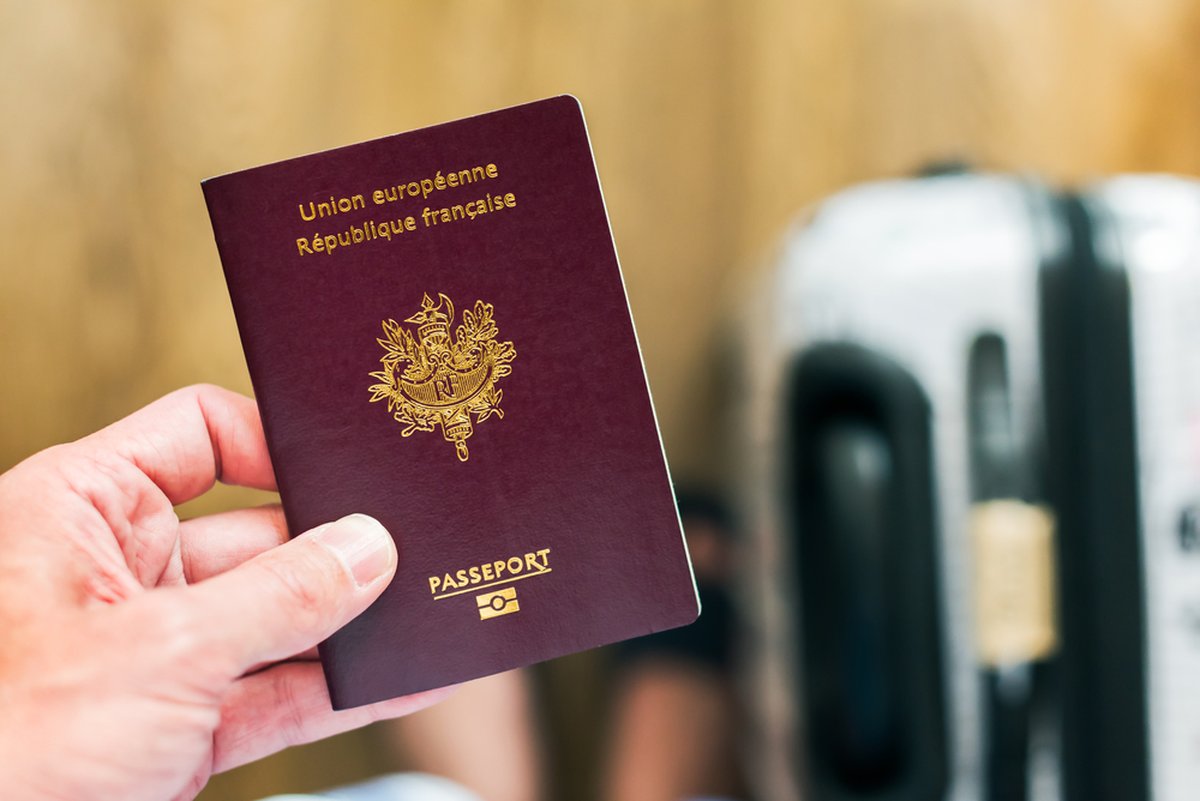 Main tenant un passeport français, prêt pour un voyage en Islande avec une valise en arrière-plan.