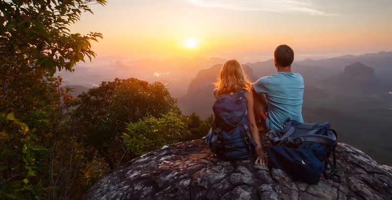 Couple de randonneurs assis sur un rocher face au coucher de soleil en montagne.