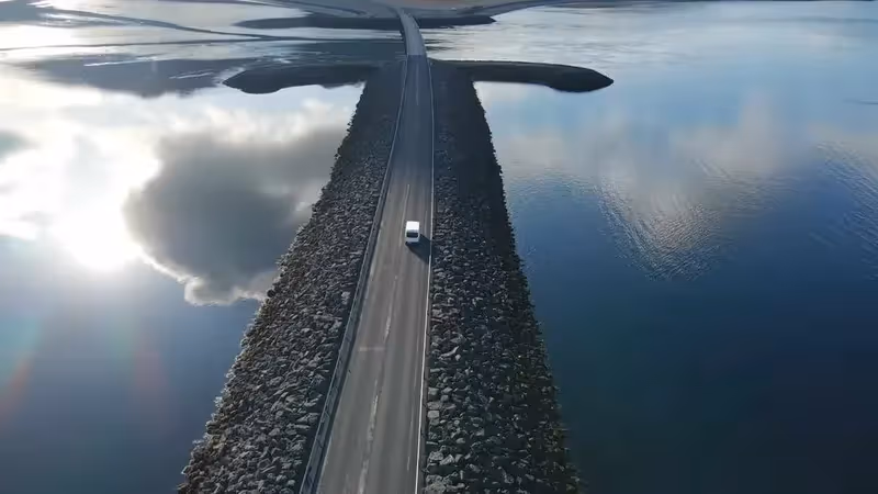 Route en Islande traversant l’océan avec une voiture blanche au centre