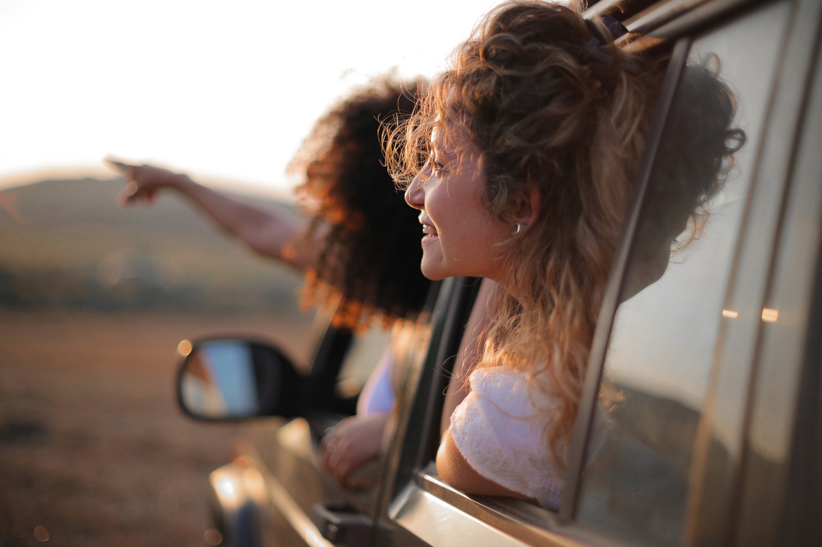 Deux amies profitant d’un road trip, la tête sortie de la fenêtre d’une voiture au coucher du soleil