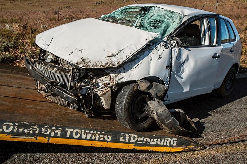Voiture blanche gravement accidentée avec avant détruit et pare-brise fissuré.
