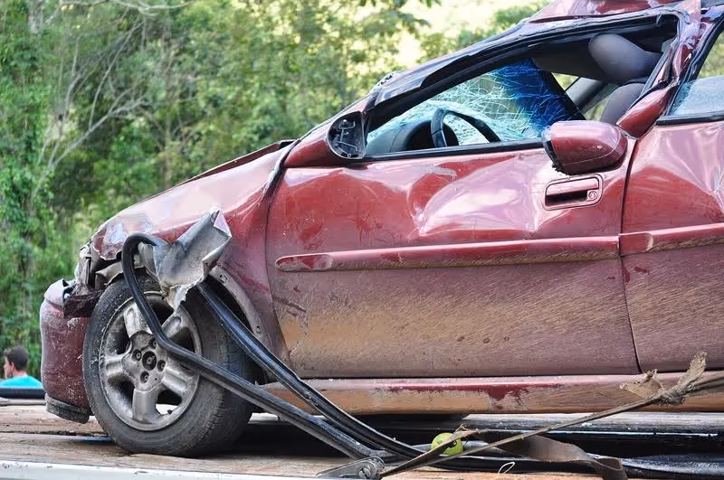 Voiture rouge fortement accidentée avec pare-brise brisé et carrosserie déformée.