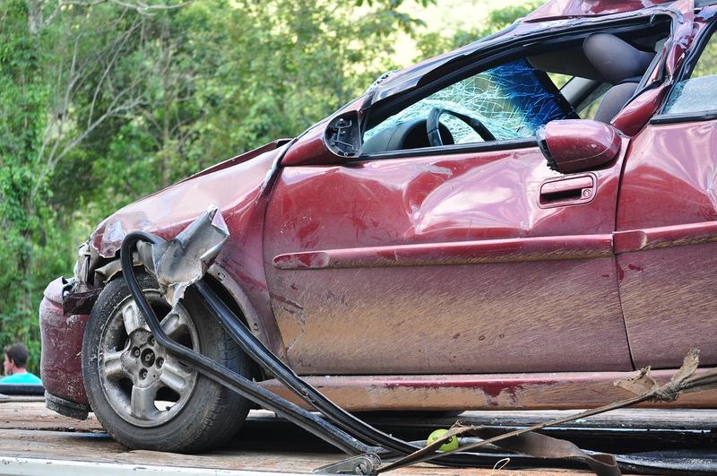 Voiture rouge fortement accidentée avec pare-brise brisé et carrosserie déformée.