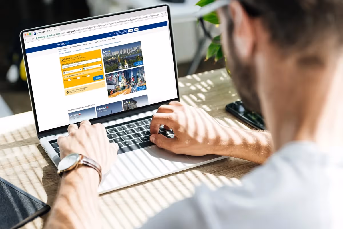 Homme consultant le site Booking.com sur un ordinateur portable pour réserver un hébergement en ligne.