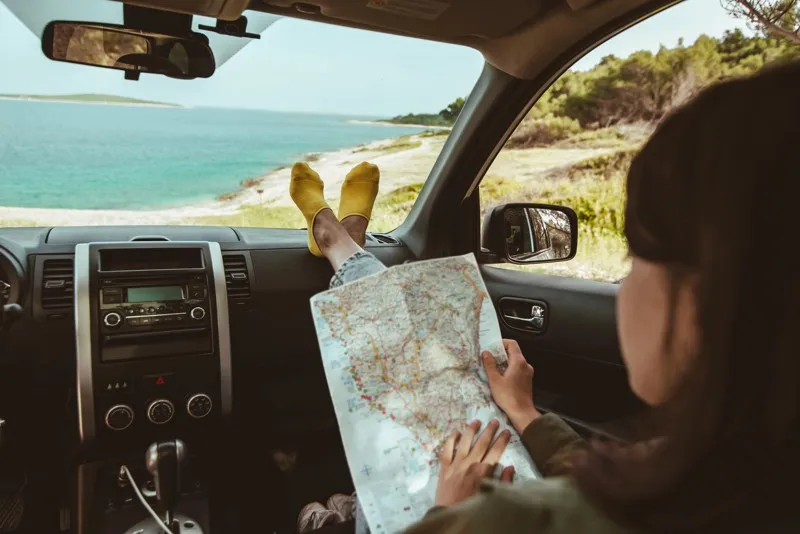 Personne assise dans une voiture au bord de la mer lisant une carte pendant un road trip