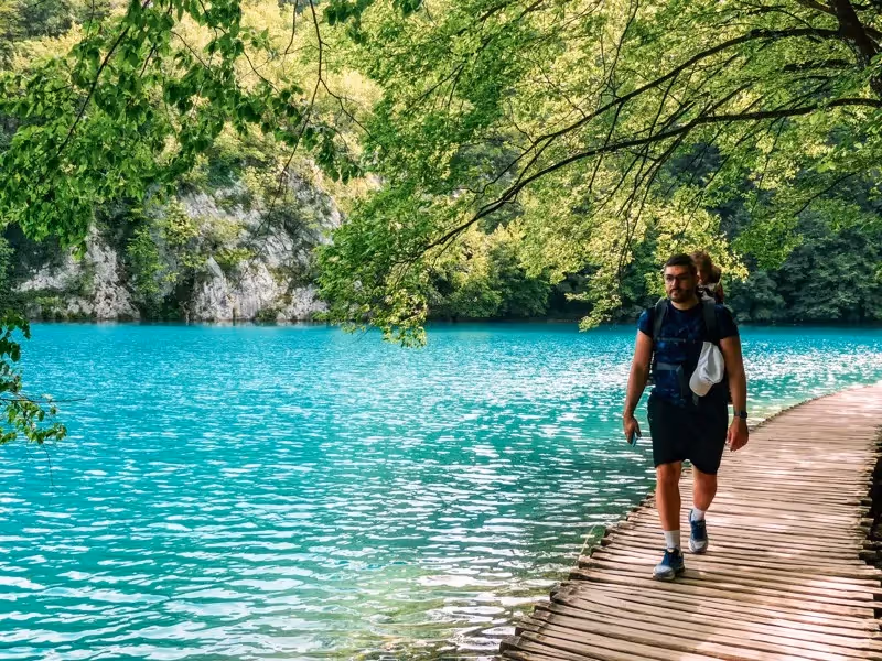 Homme marchant sur un ponton en bois au bord des lacs turquoise du parc national de Plitvice en Croatie.