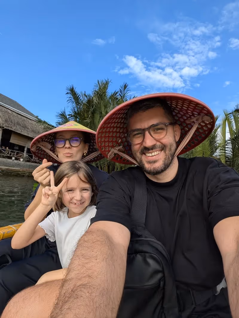 Famille souriante en bateau panier à Hoi An, Vietnam, portant les chapeaux traditionnels vietnamiens.