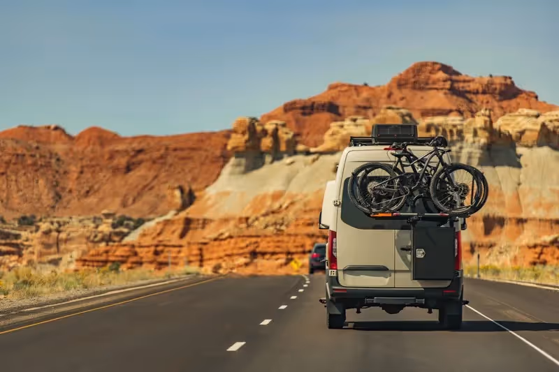 Fourgon aménagé roulant sur une route du désert américain, symbole de liberté et d’aventure.