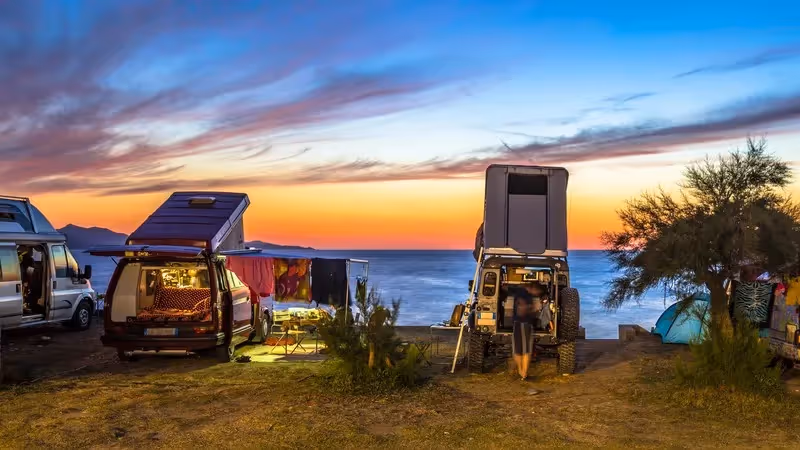 Vans aménagés stationnés en bord de mer au coucher du soleil, parfaits pour un road trip en liberté.
