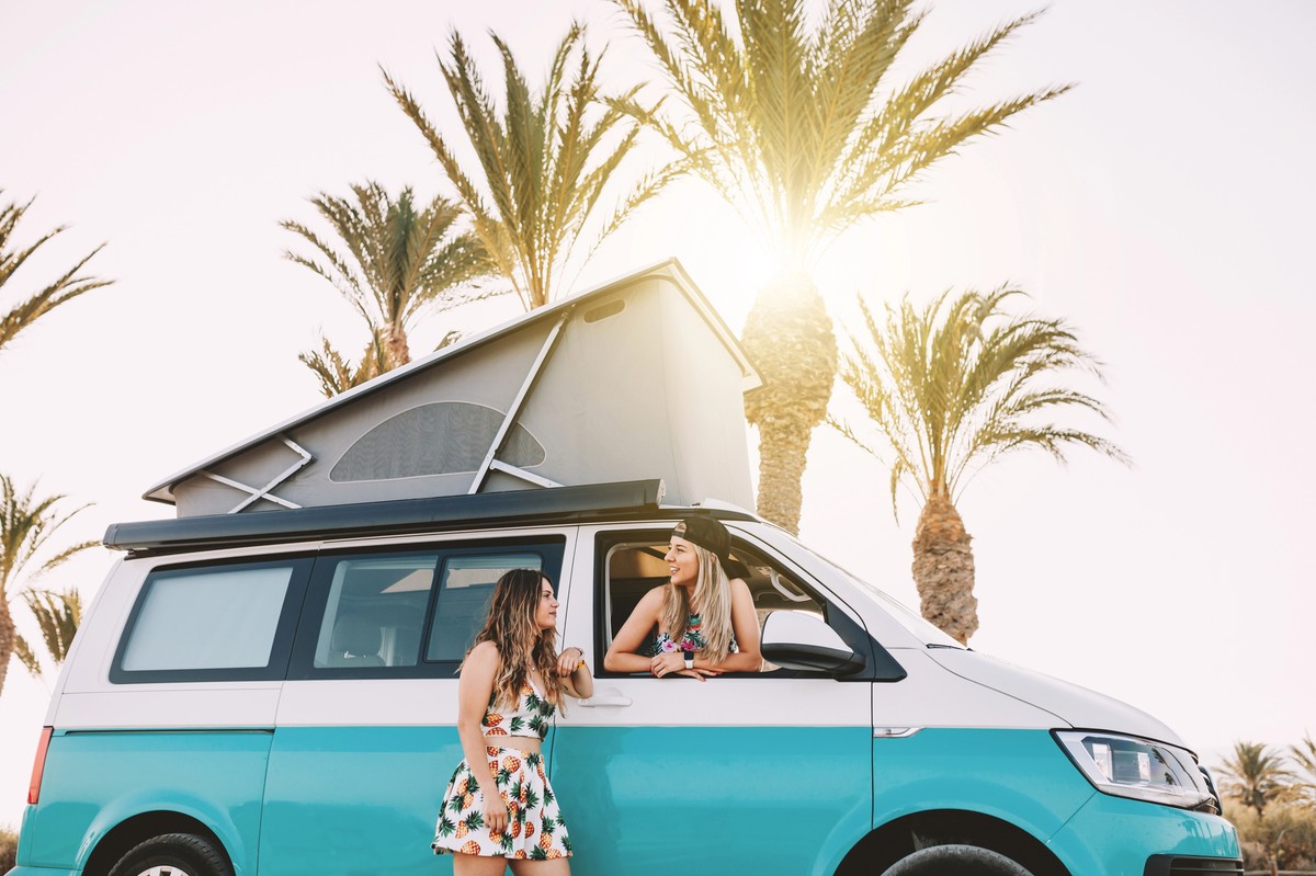 Van aménagé turquoise garé sous des palmiers, symbole de liberté et de voyage au soleil.