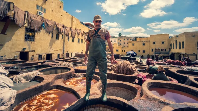 Ouvrier dans les tanneries traditionnelles de Fès, Maroc, entouré de cuves colorées de teinture.