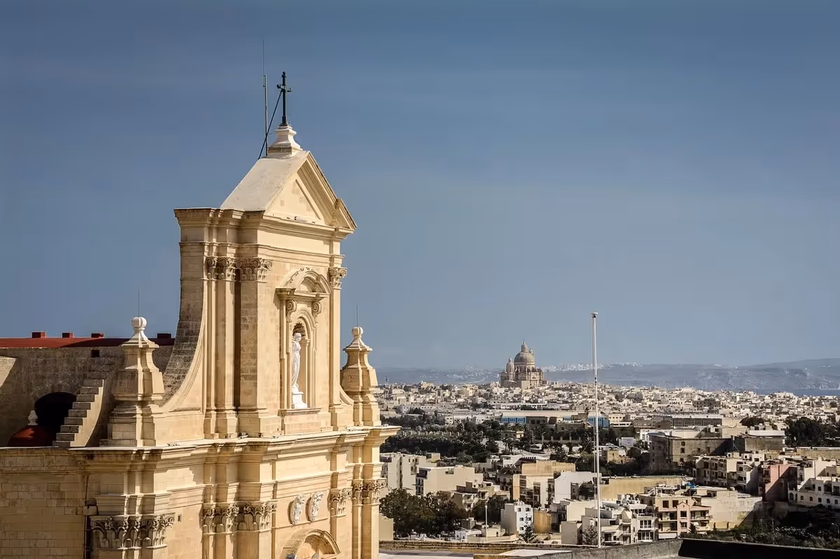 Façade de la Citadelle de Victoria à Gozo avec vue lointaine sur la basilique Ta’ Pinu et les paysages urbains maltais.