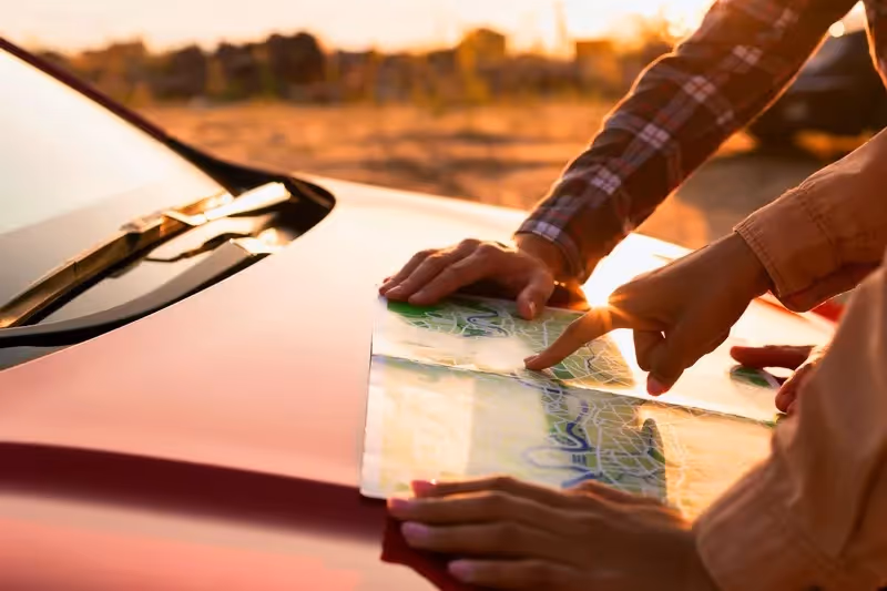 Deux personnes consultent une carte posée sur le capot d’une voiture au coucher du soleil lors d’un road trip.