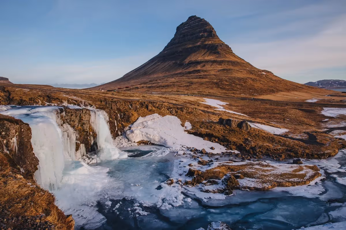 Vue sur la montagne Kirkjufell et les chutes gelées de Kirkjufellsfoss en Islande, photographiées en hiver avec des zones de glace et de neige.