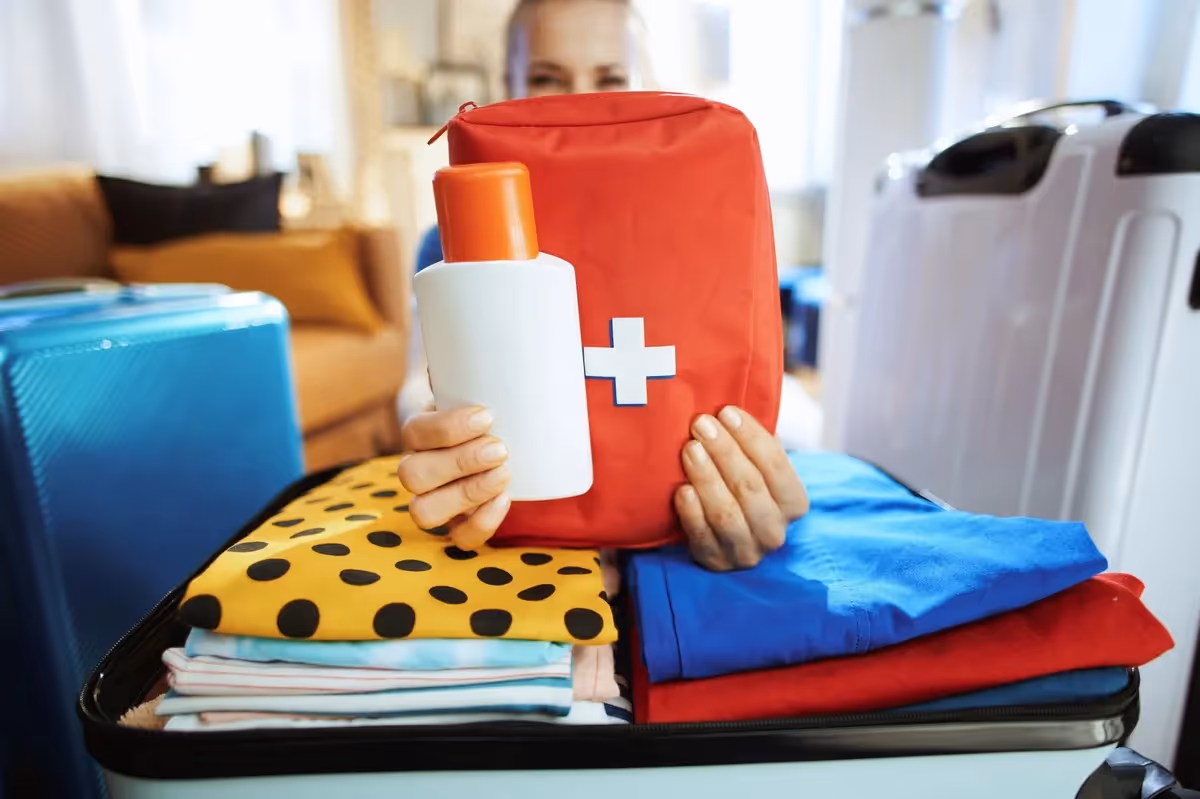 Trousse de premiers secours rouge et bouteille de lotion tenues au-dessus d’une valise en cours de préparation.