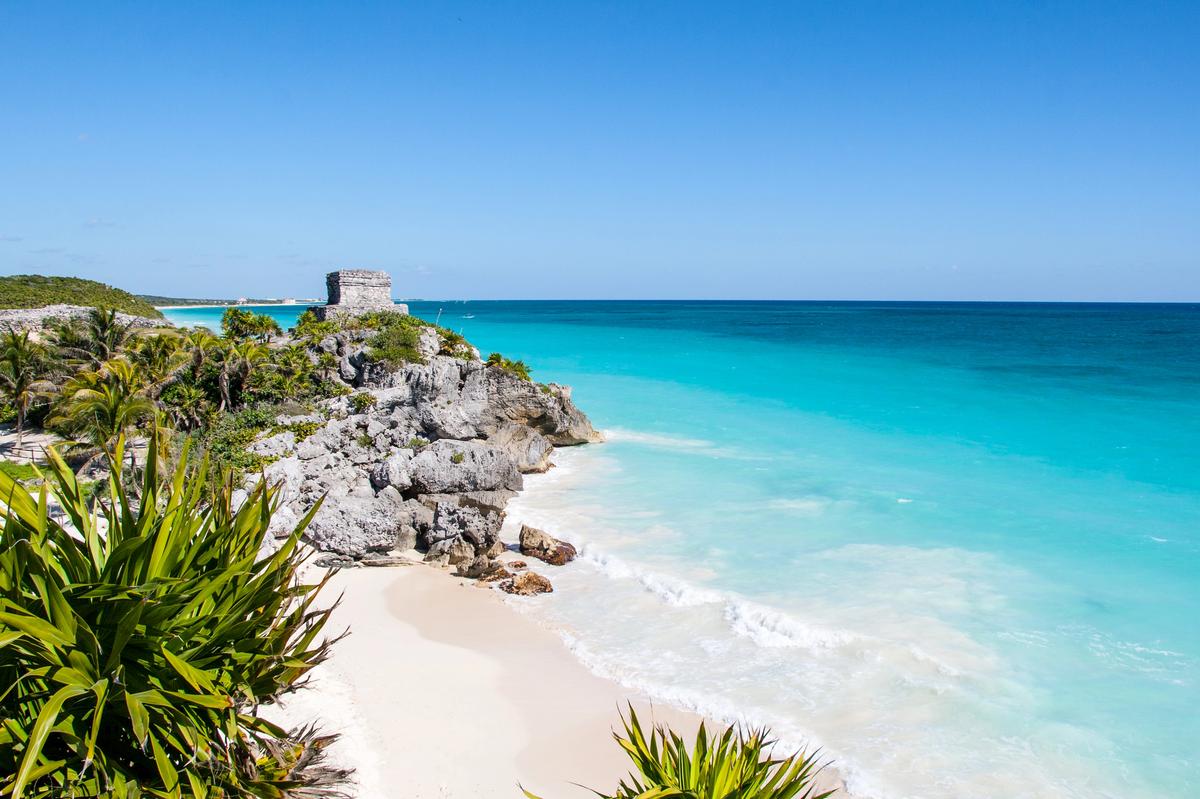 Vue emblématique des ruines mayas de Tulum surplombant une plage de sable blanc et la mer turquoise de la Riviera Maya au Mexique.