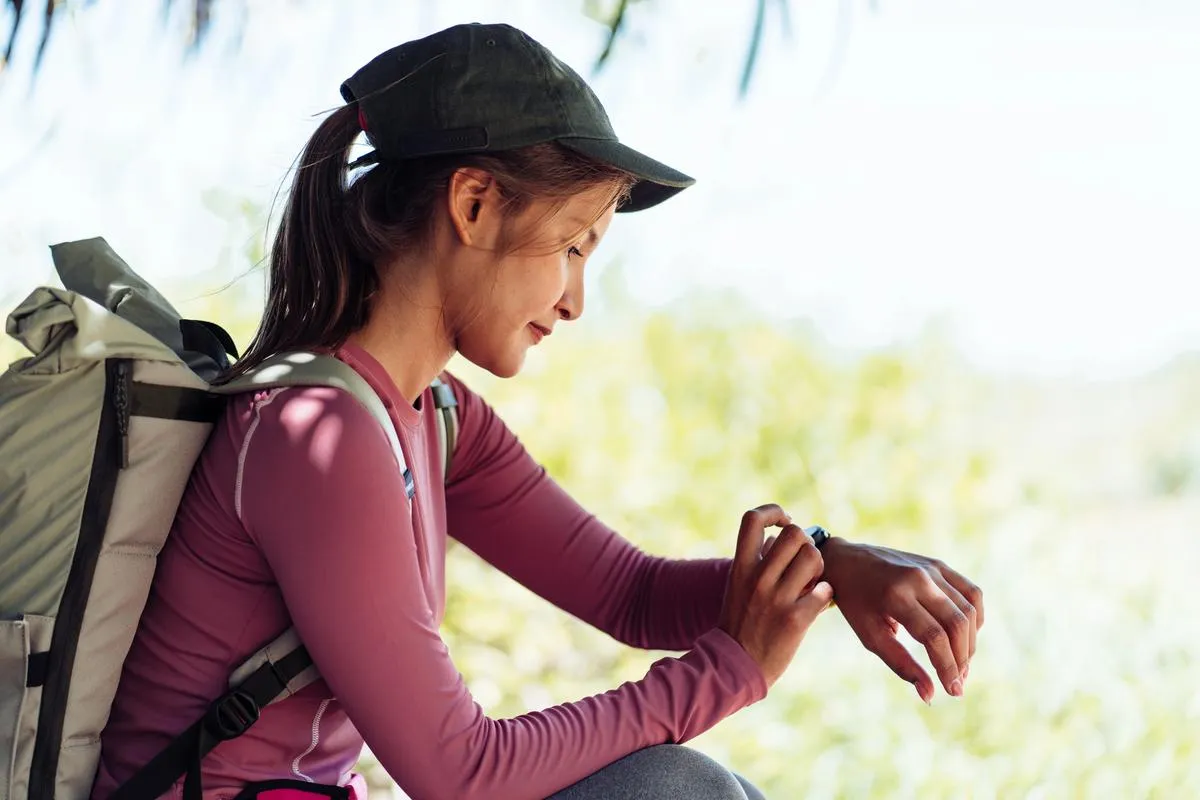 Jeune randonneuse consultant sa montre connectée en pleine nature pendant un voyage.