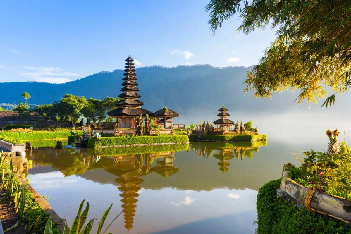 Temple Ulun Danu Beratan à Bali, posé sur un lac calme avec une montagne en arrière-plan et une lumière matinale douce.