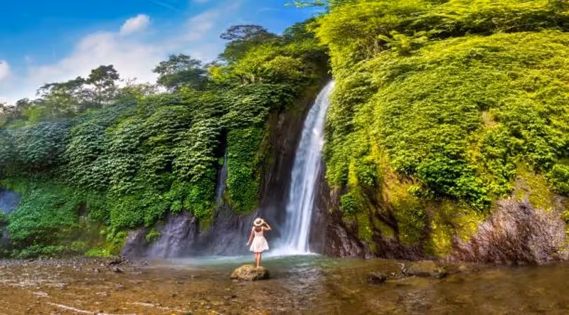 Voyageuse debout sur un rocher devant une grande cascade entourée d’une jungle dense à Bali.