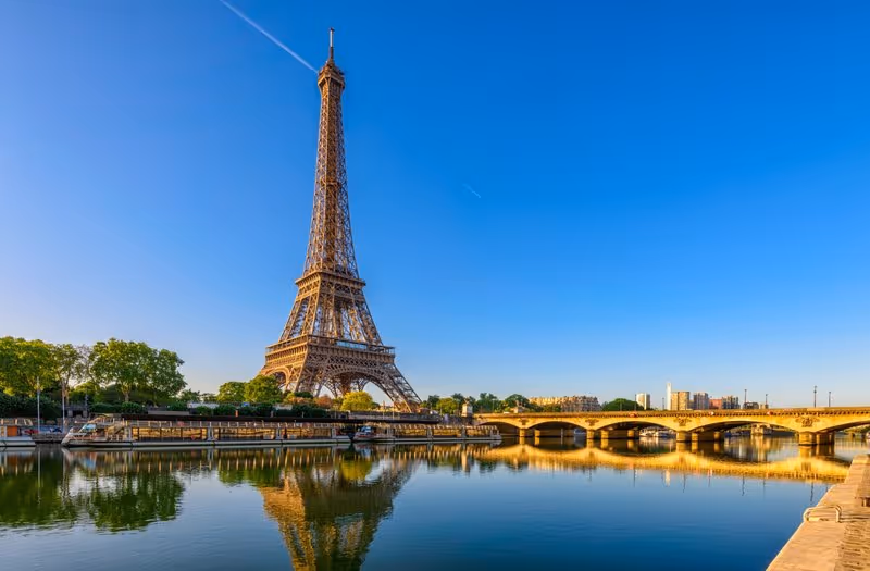 La tour Eiffel se reflétant dans la Seine par temps clair, avec un pont parisien au premier plan.