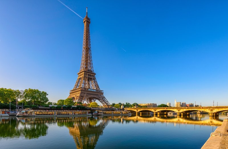 La tour Eiffel se reflétant dans la Seine par temps clair, avec un pont parisien au premier plan.