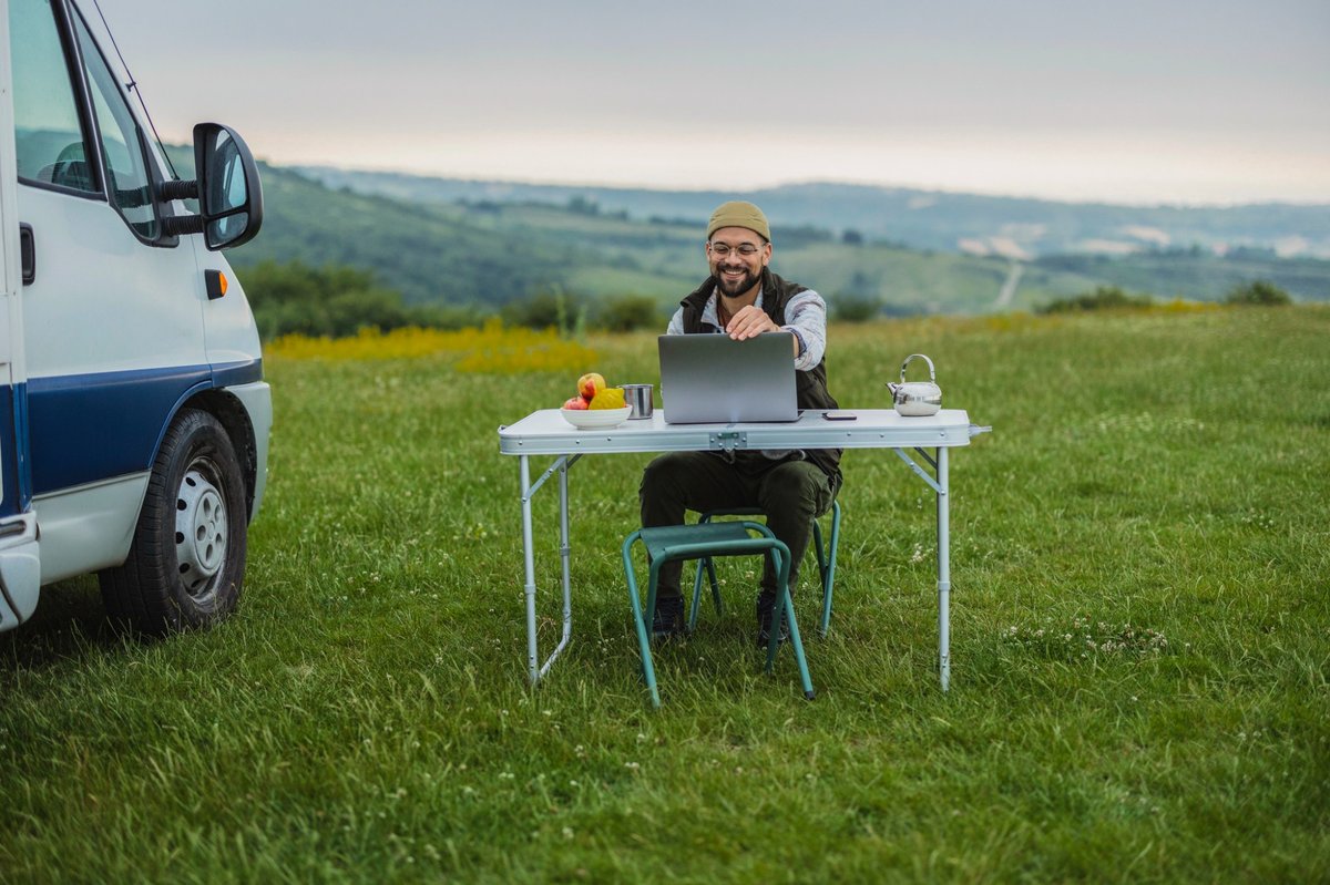Nomade digital travaillant à distance depuis un van aménagé, ordinateur portable posé sur une table en pleine nature