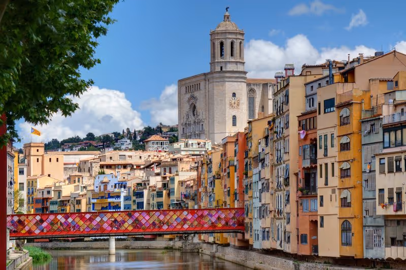 Maisons colorées de Gérone alignées le long de la rivière Onyar, avec la cathédrale de Girona en arrière-plan et le pont rouge emblématique.